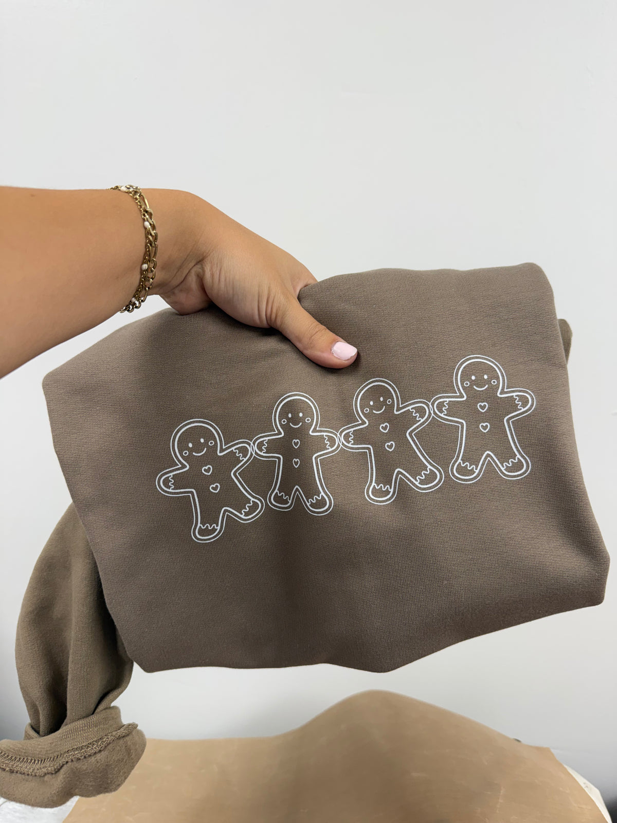 a person holding a brown sweater with gingerbread men on it